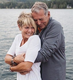 portrait of an older couple hugging with a lake in the background