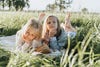 Blonde sisters lying on stomachs in grass barefoot with book