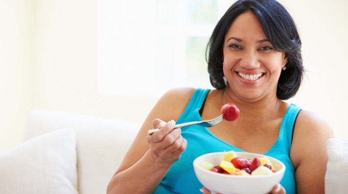 happy woman sitting on couch eating a bowl of fruit