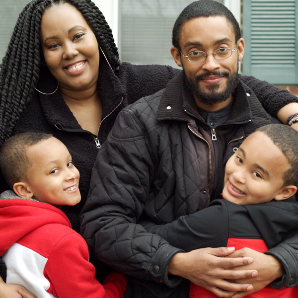 чернокожий мужчина в очках обнимает жену и детей
