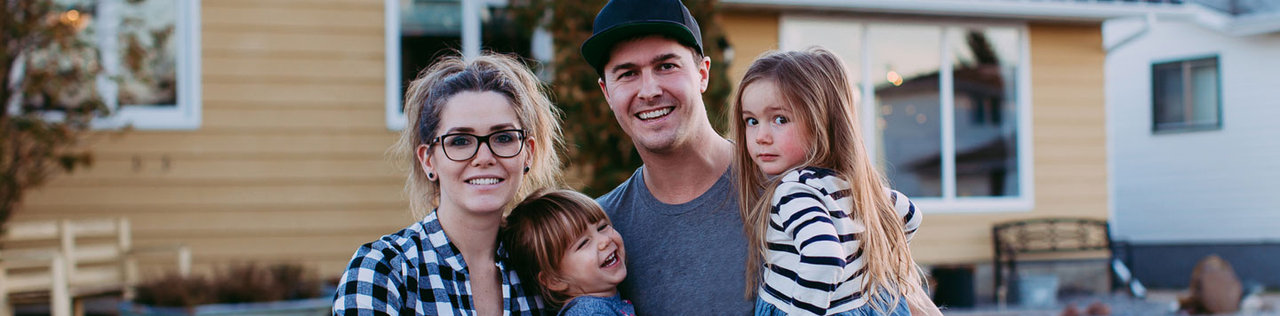 Family of four smiling together outside their home.