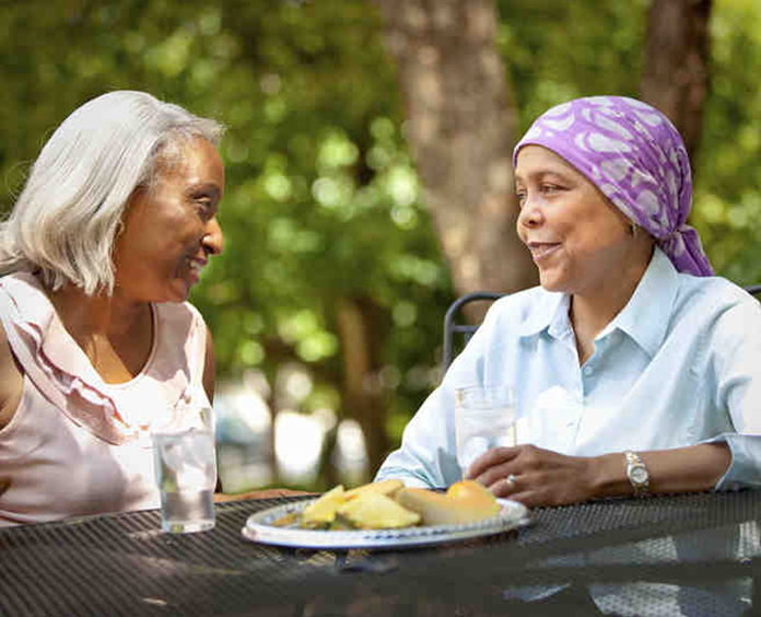 Woman with head wrap talking with a Reach To Recovery volunteer at an outside table.