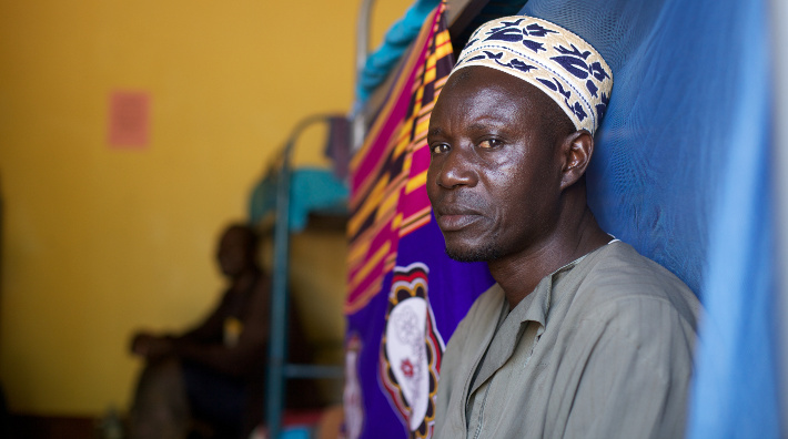 Male patient sitting on bed in Uganda hostel