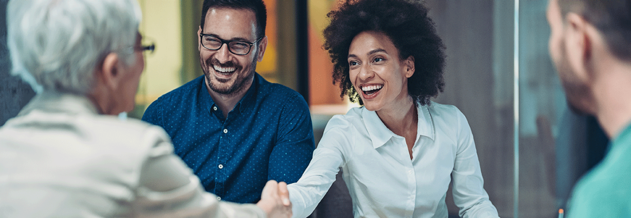 Professionals smiling and shaking hands in a meeting.