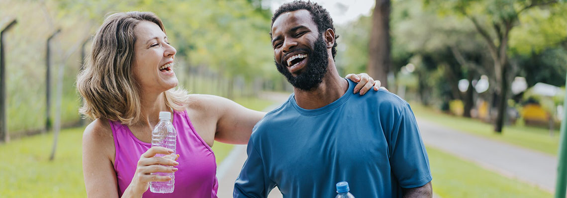 A female in pink shirt and a male in a blue t shirt laughing while on a walk outdoors