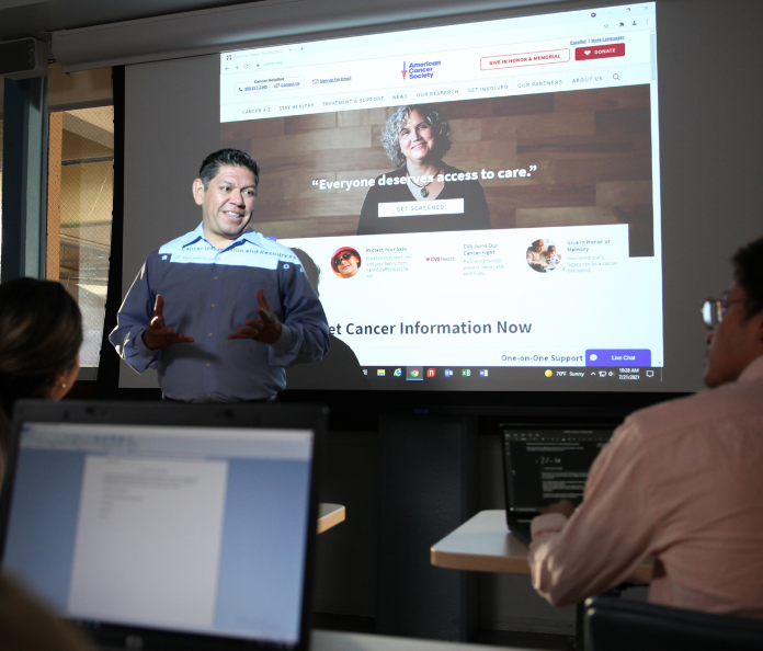 hispanic male wearing light blue button down shirt presenting in classroom