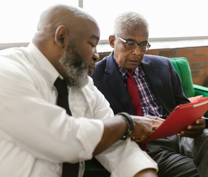 Two senior black men talking on a green couch