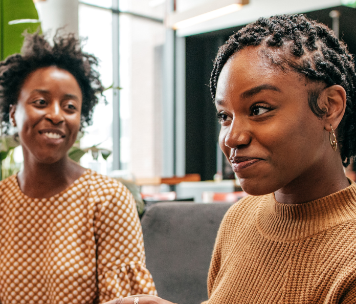 Two black women smiling sitting on couch