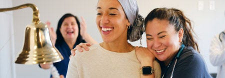 A cancer survivor rings bell surrounded by loved ones and doctors