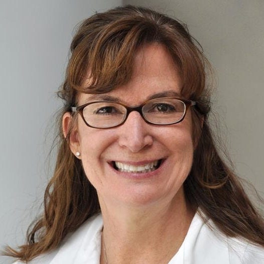 Woman with auburn hair behind shoulders and oval glasses in lab coat