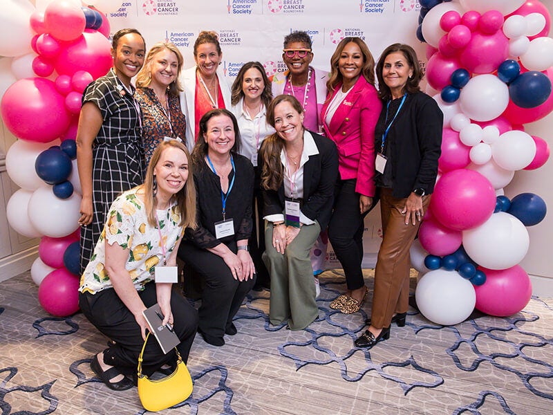 Group of women posing at breast cancer event backdrop balloons.