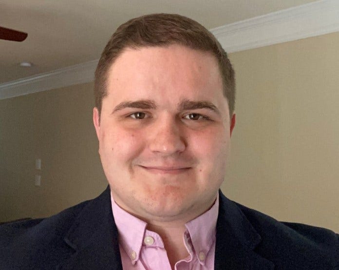 white man with short brown hair, pinky/purple shirt and black jacket 