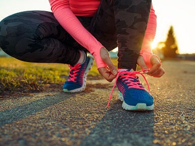 A person ties a sneaker with pink laces, sun shines from behind