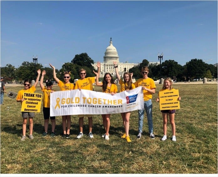 group of people all wearing gold shirts standing in front of capital