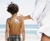 a mother applies sunscreen to her son's back at the beach