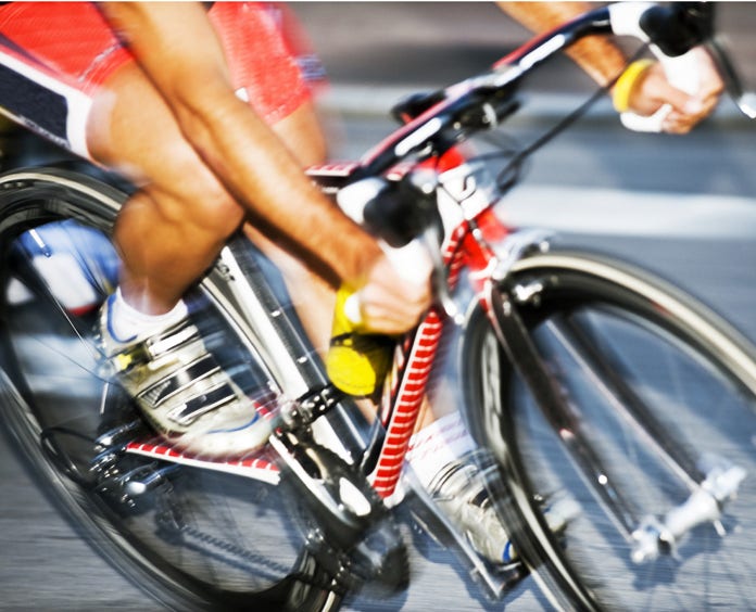 A bike with a racer riding it that is blurred from speed going down a road