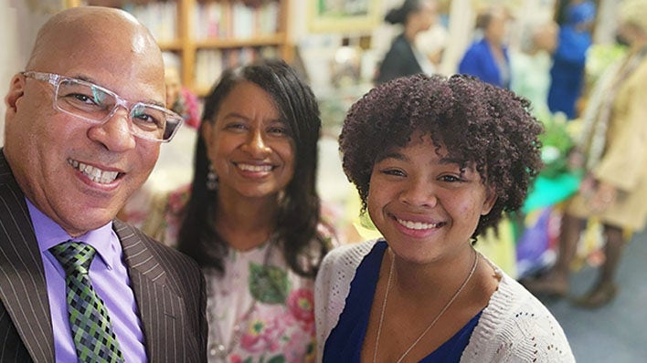 Three smiling people posing together at an indoor event.