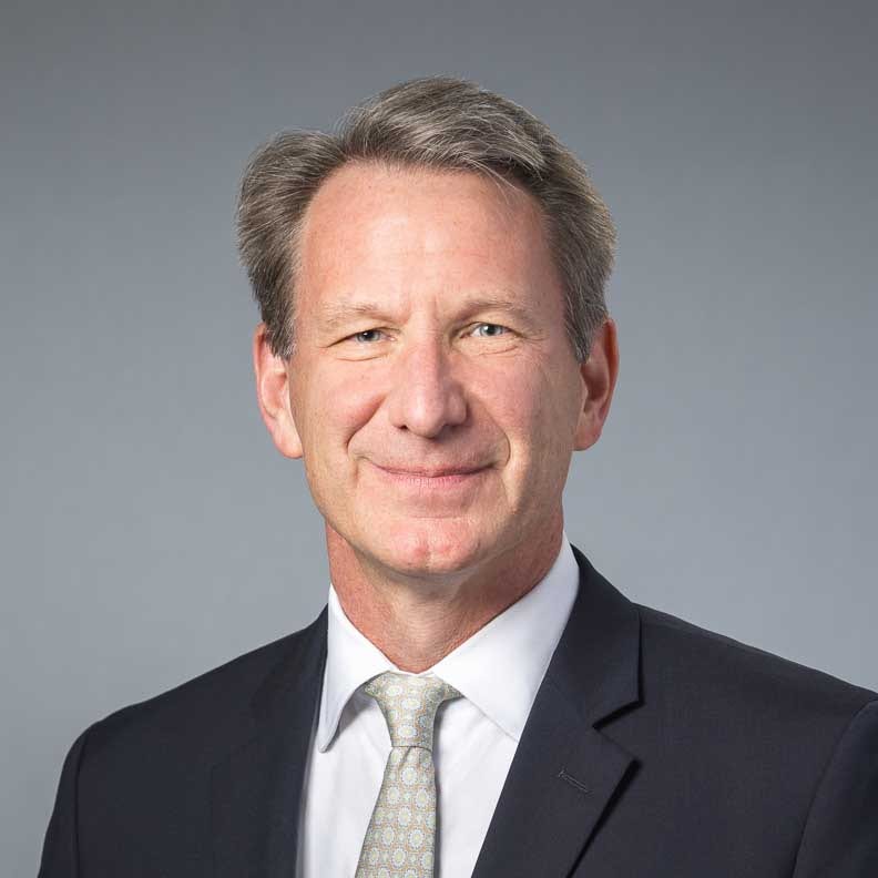 Smiling man in dark suit with patterned tie.