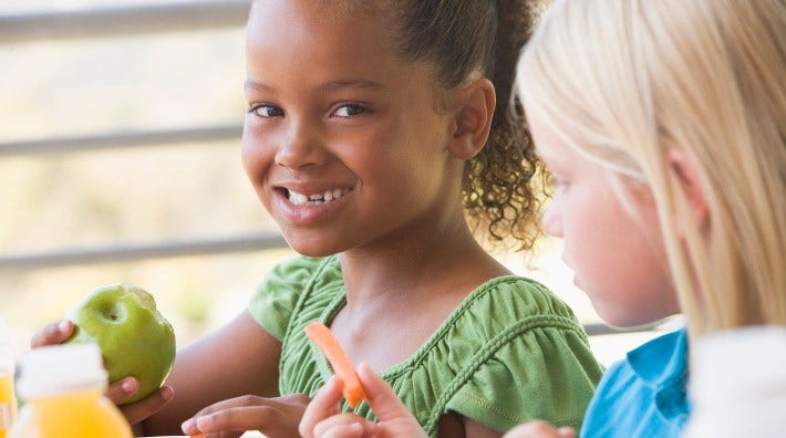 happy little girl eating an apple from her lunch box