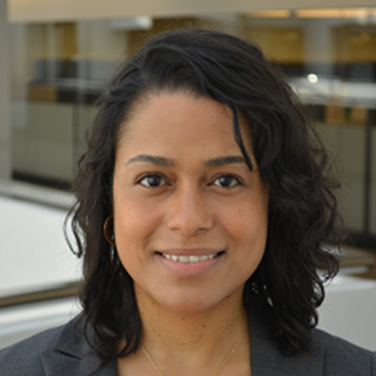 headshot of woman with dark wavy hair with office windows behind her