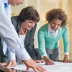 A group of executives with plans spread out on a table discussing them.