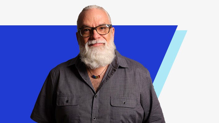 Man with glasses and a white beard posing in front of a blue background
