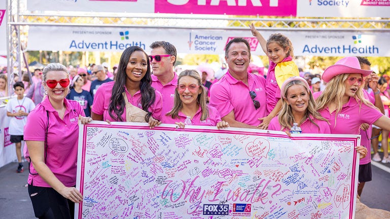 Group of participants at the Making Strides Against Breast Cancer event hold a large signature-covered support board near the start line.