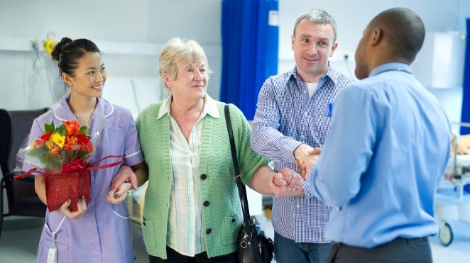 senior woman and her son leaving hospital with help of nurse and doctor