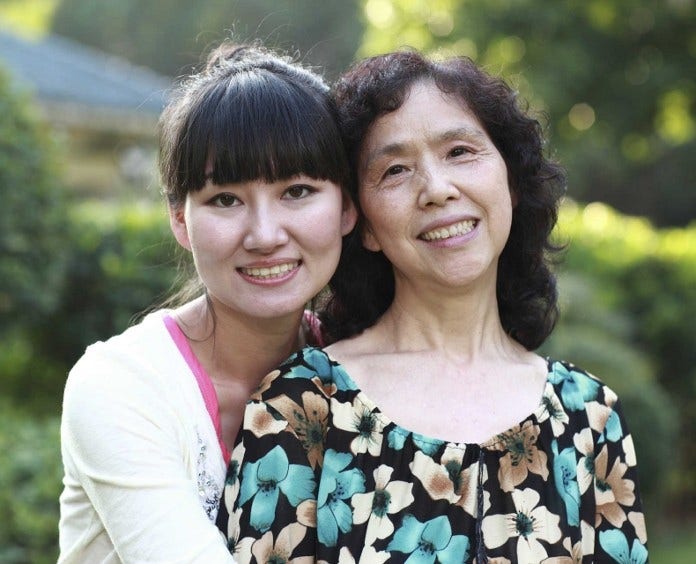 young woman and her mother embrace outside and smile to camera