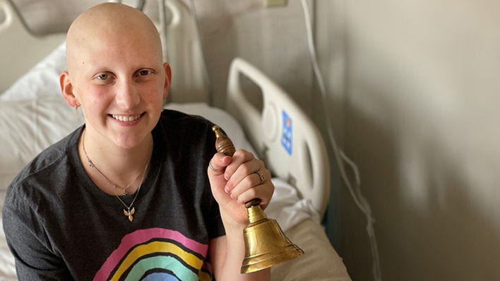 Young cancer patient smiling and holding a bell in a hospital room