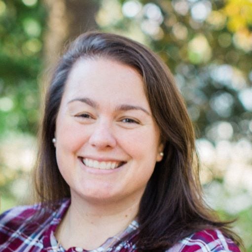 White woman outside brown hair, parted on left, pearl earrings, red  plaid shirt