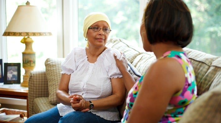 cancer patient in headscarf is comforted by a caregiver sitting next to her