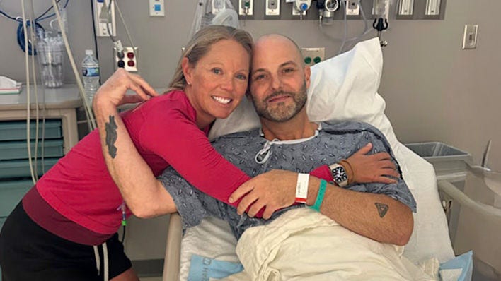 Mujer abrazando a un hombre en una cama de hospital, ambos sonriendo.