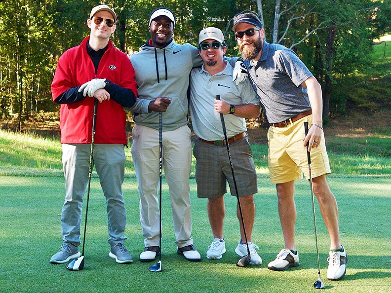 Four men with golf clubs standing together at an ACS golf event