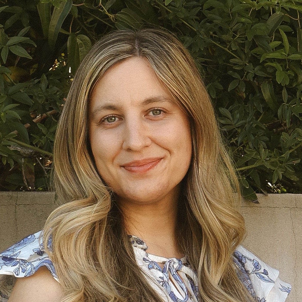 white young woman with long blonde hair in blue and white dress in front of concrete wall and tree