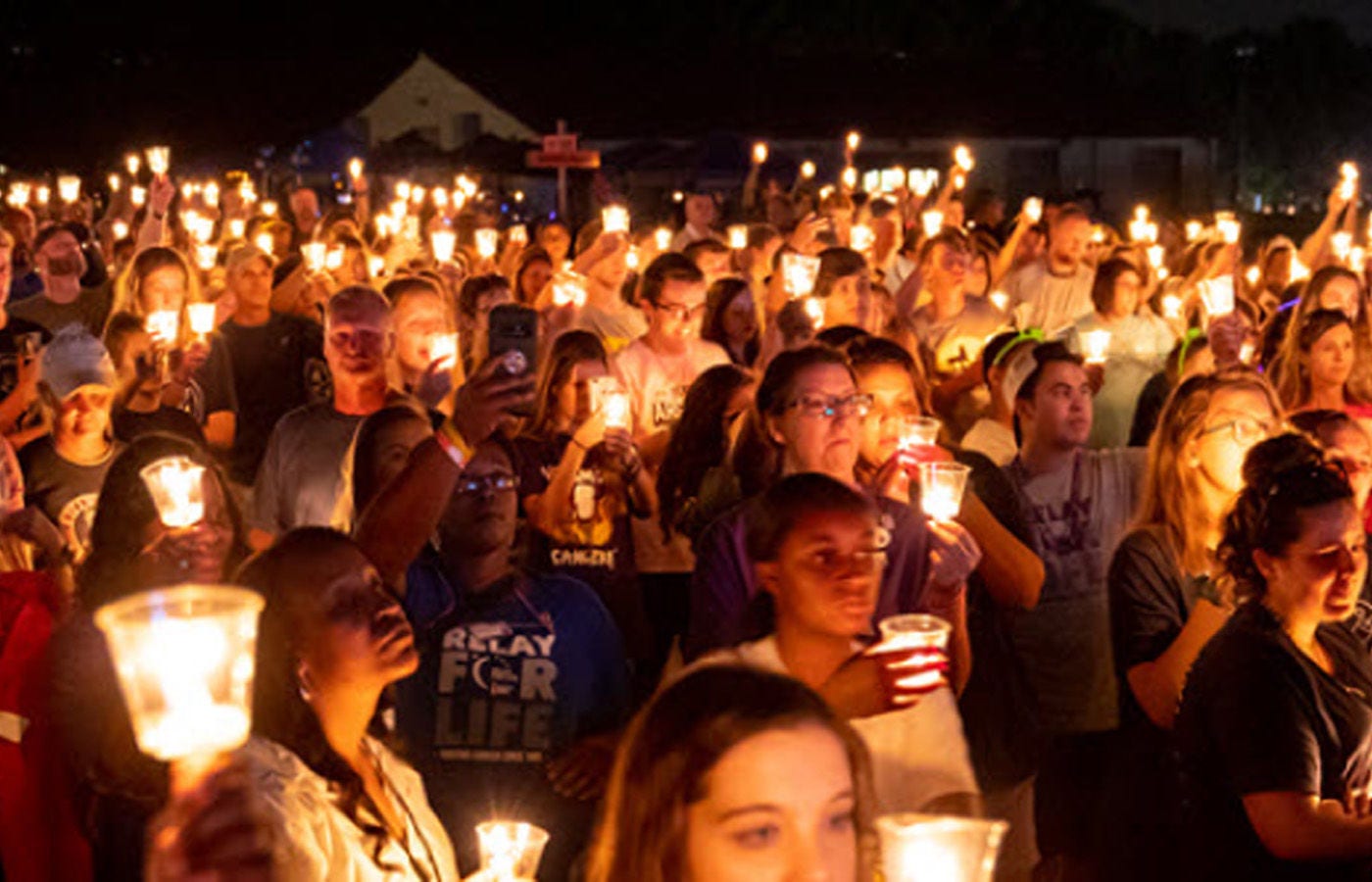 Wide shot of group of people at an event during night-time holding up a light