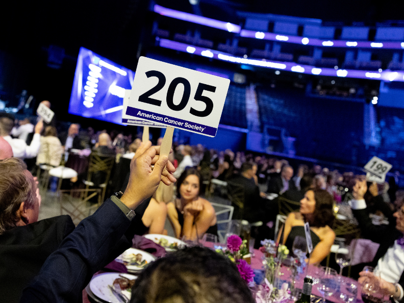Audience member raising numbered paddle at charity gala.