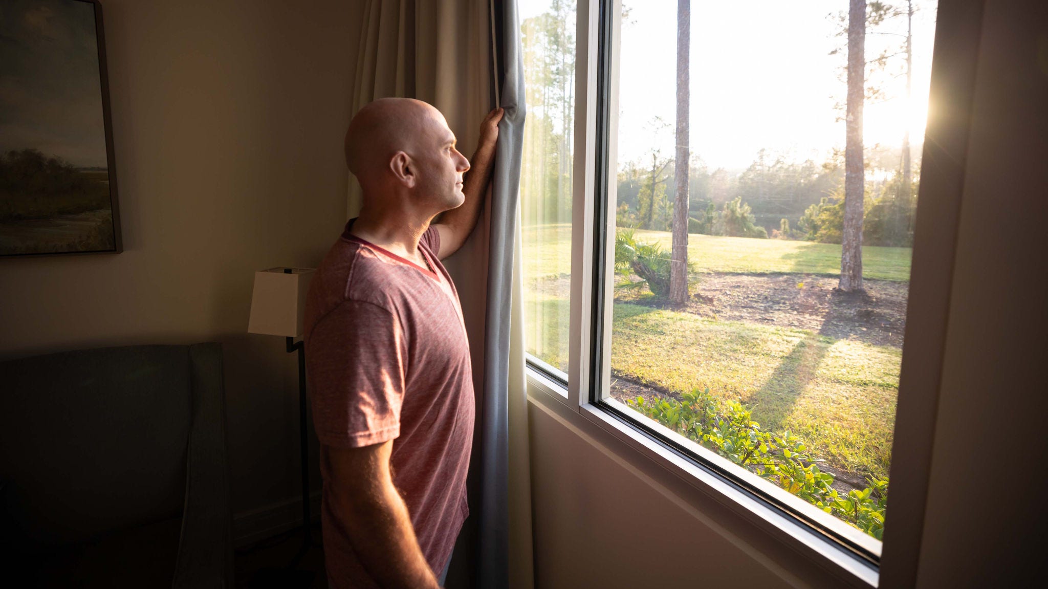 Hombre mirando por la ventana hacia la luz del sol y los árboles afuera.