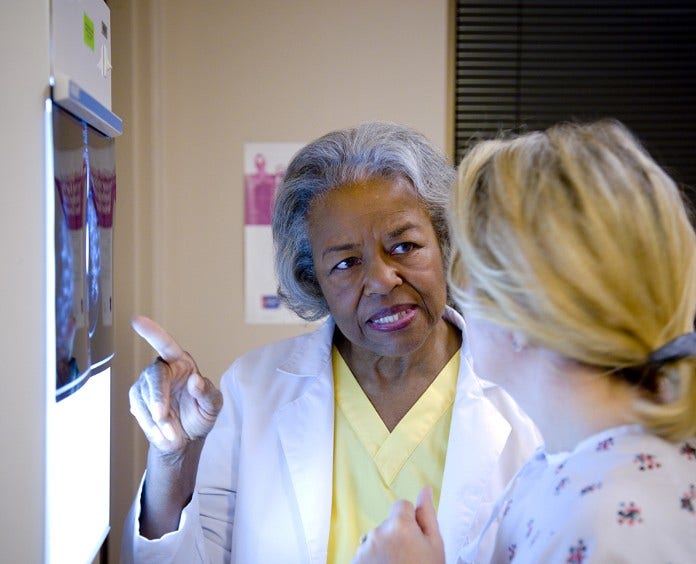An older African American female doctor discusses a mammogram with a blonde female patient
