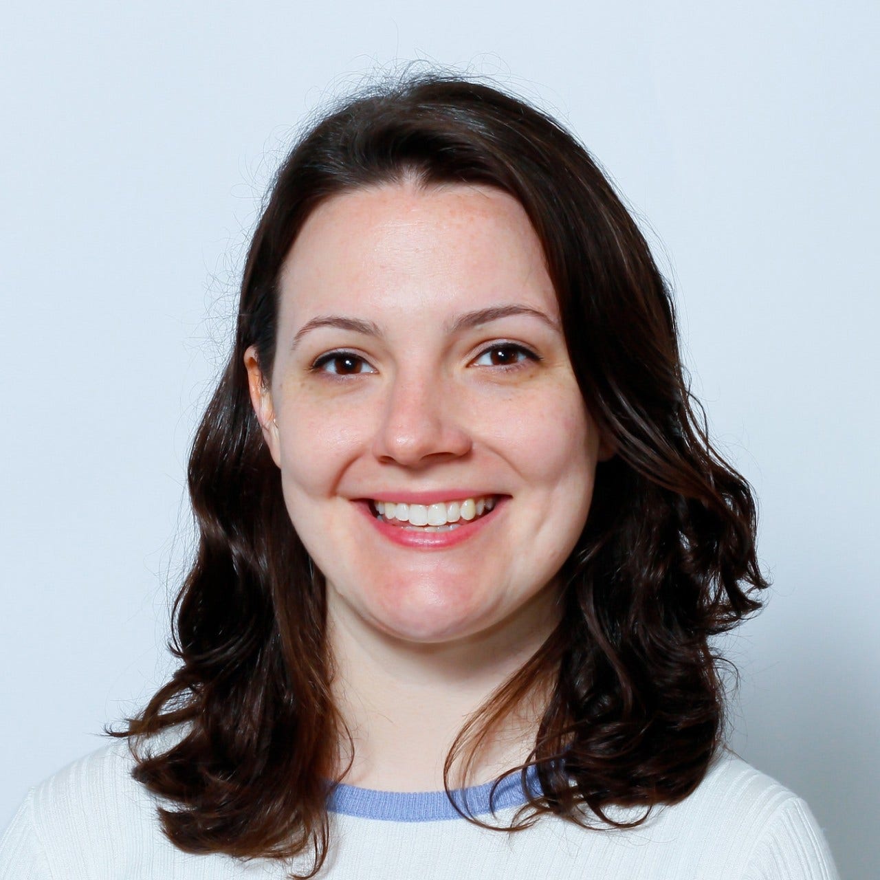 white woman, dark shoulder-length hair, white sweater with light blue neckline