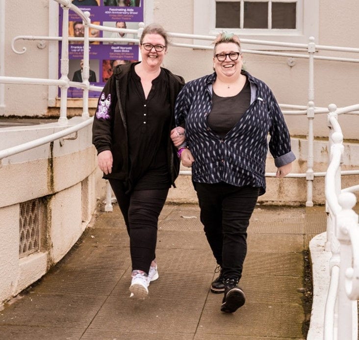 two large women walking arm in arm inside dressed in black smaller size