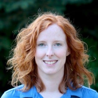 woman with red, shoulder-length hair in bright blue shirt in front of dark green background