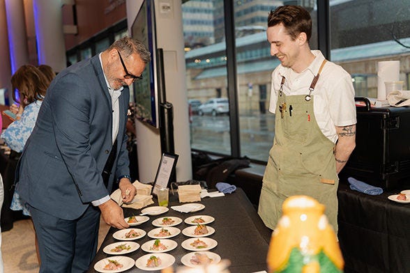 Man serving small plated dishes while another smiles at a table.