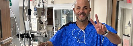 Hospital patient standing in a medical unit and holding up a peace sign.