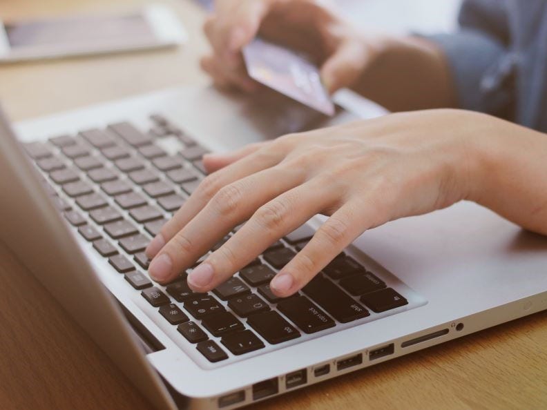 A laptop with hands typing and holding a credit card