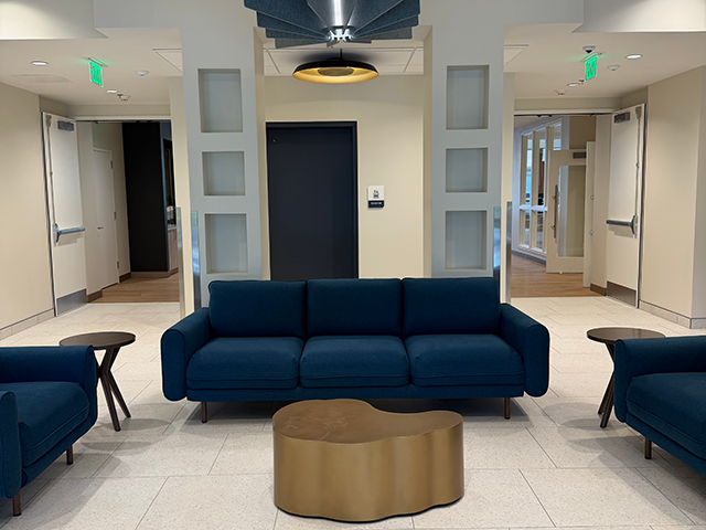 Modern lobby with blue sofas, gold table, and central elevator.