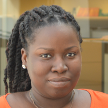 Black woman hair pulled in pony tail, orange shirt, triangles necklace