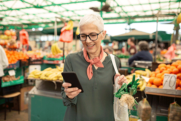 Smiling woman shopping at market while using phone.