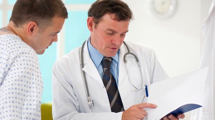 a doctor goes over paperwork with a patient in gown in an exam room