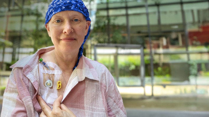 Mujer muestra su puerto de quimioterapia, usando un pañuelo azul en la cabeza